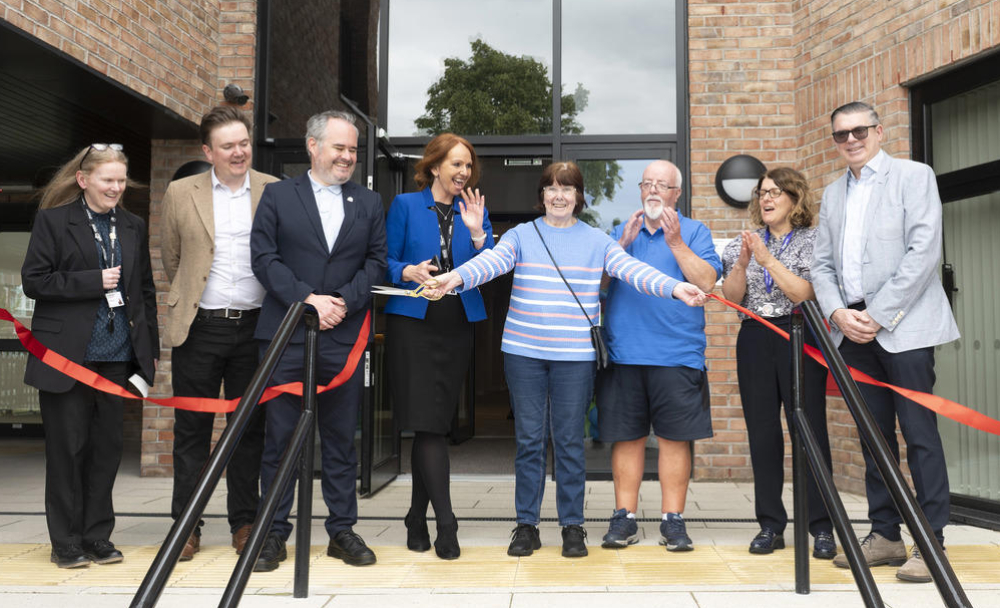 People gather to cut a ribbon in front of a buff coloured brick building called Brookhead Lodge that is now officially open.